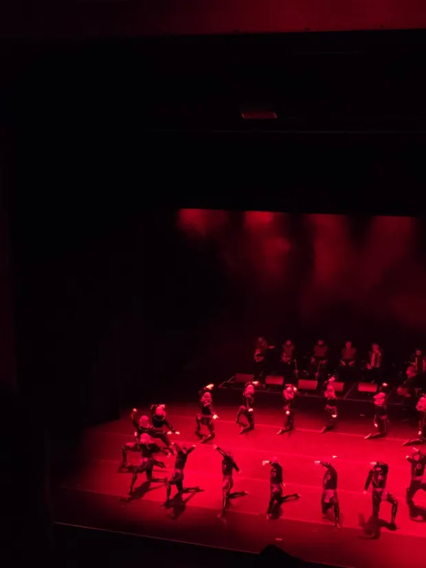 Dancers in dark costume lunging and kneeling across a stage saturated in red light