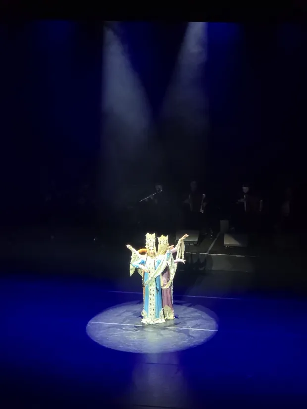 The three crowned dancers close together with arms fanned at different heights, musicians faintly visible behind
